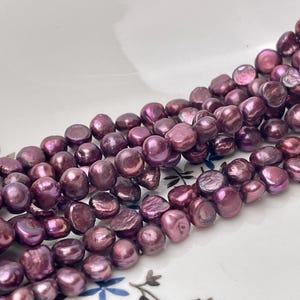 May include: Strands of lustrous, deep purple freshwater pearls. The pearls have an irregular, organic shape and a shimmering, iridescent quality. The beads are arranged in multiple strands, suggesting their use in jewelry making.