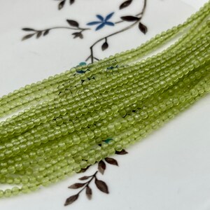 May include: A strand of light green peridot beads, each bead is faceted and has a slightly irregular shape.