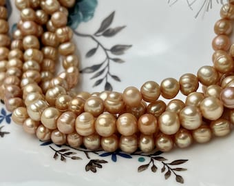 May include: A strand of golden pearls with a slight pink hue. The pearls are round and have a smooth, iridescent finish.
