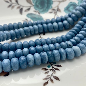 May include: A strand of light blue round beads with a speckled texture. The beads are arranged in a circular pattern on a white surface.