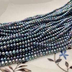 Może przedstawiać: Sznur iryzujących niebieskich i zielonych pereł słodkowodnych. Perły są okrągłe i gładkie, a nawleczone są na przezroczystą nić.