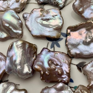 May include: Irregular-shaped, iridescent pearls in shades of brown, gray, and white. The pearls have a unique, organic form, with a lustrous surface. These natural pearls are ideal for jewelry making.