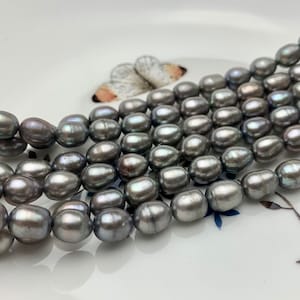 May include: A strand of gray freshwater pearls, with a slightly iridescent sheen. The pearls are oval shaped and have a smooth, polished surface.