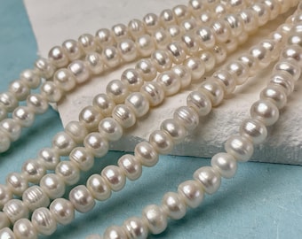 May include: Strands of creamy white pearls, each with a slightly irregular shape, are displayed. The pearls are strung together, creating a necklace or bracelet. The background is a light blue surface.