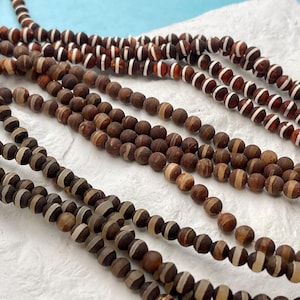 May include: A close-up of several strands of brown and white agate beads. The beads are round and have a natural, polished finish.