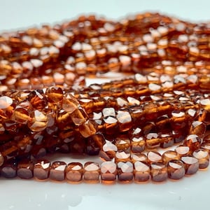 May include: A strand of brown gemstone beads with a faceted, square shape. The beads are strung together to create a necklace or bracelet.