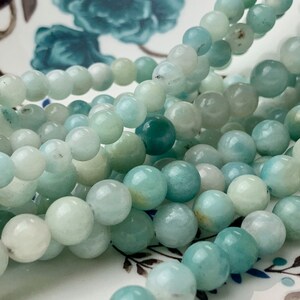 May include: A strand of light blue and green aquamarine beads. The beads are round and smooth, and they are strung on a clear thread.
