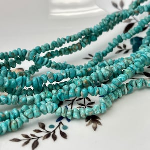 Puede incluir: Primer plano de múltiples hebras de cuentas de virutas de turquesa. Las cuentas son de un color turquesa vibrante con inclusiones de matriz marrón. Las hebras están dispuestas en un patrón en capas, mostrando la textura y las variaciones de color de la piedra natural.