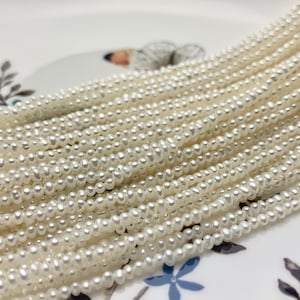 Puede incluir: Una hebra de perlas de agua dulce blancas, con una forma redonda y lisa. Las perlas están enhebradas en un hilo fino y todas son de tamaño aproximadamente igual.