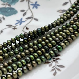 May include: A strand of dark green freshwater pearls, with a slight iridescent sheen. The pearls are round and smooth, and they are strung on a clear thread.