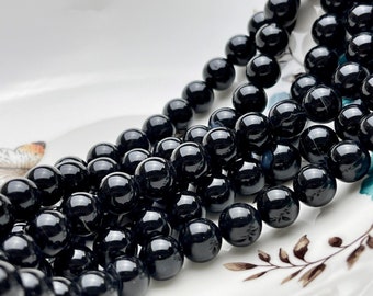 Puede incluir: Una hebra de cuentas de piedras preciosas negras, probablemente obsidiana u ónix, con un acabado liso y pulido. Las cuentas son redondas y de tamaño uniforme, creando un aspecto consistente.