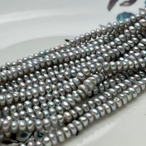 Peut inclure: Un brin de perles d'eau douce grises, avec un léger éclat iridescent. Les perles sont de forme ovale et ont une finition lisse et polie.