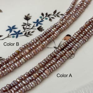 May include: Close-up of two strands of small, light purple freshwater pearls. The pearls are strung together, with the text "Color A" and "Color B" labeling each strand. The pearls are on a white plate with blue floral designs.