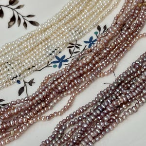 Può includere: Primo piano di più fili di piccole perle a forma di seme nei toni del bianco, rosa e viola. Le perle sono infilate insieme, creando un effetto strutturato e stratificato. Lo sfondo è un piatto bianco con disegni floreali.