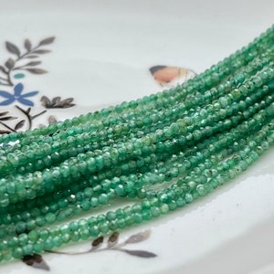 Peut inclure: Un brin de perles d'émeraude vertes, chaque perle est facetée et a une forme légèrement irrégulière. Les perles sont enfilées sur un fil transparent et sont disposées en un motif lâche et fluide.