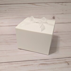 May include: A white gift box with a white satin ribbon tied in a bow on top.