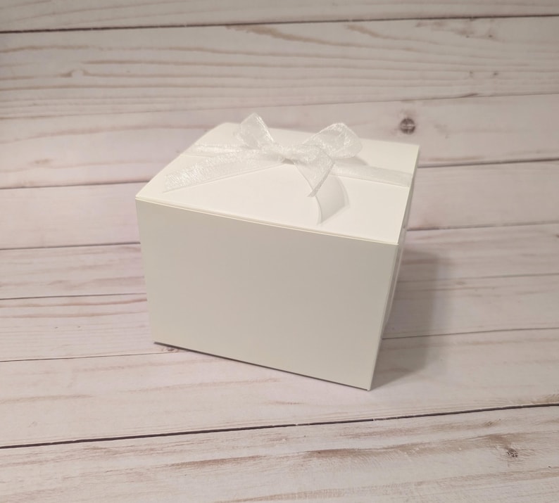 May include: A white gift box with a white satin ribbon tied in a bow on top.