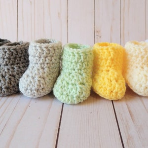 May include: A row of seven crocheted baby booties in various colors, including gray, white, light green, yellow, and cream.