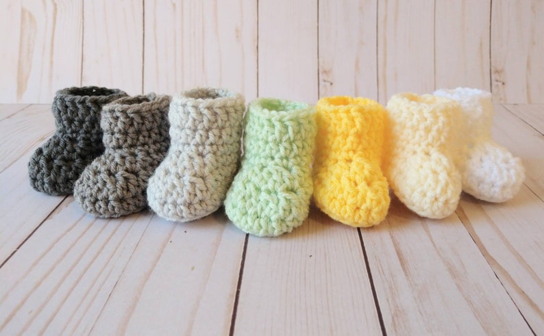 May include: A row of seven crocheted baby booties in various colors, including gray, white, light green, yellow, and cream.
