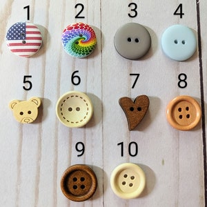May include: Ten different wooden buttons with various designs, including an American flag, a rainbow swirl, a gray circle, a light blue circle, a teddy bear, a heart, a brown circle with four holes, a beige circle with two holes, a brown circle with four holes, and a beige circle with six holes.