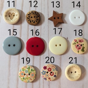 May include: Assortment of 21 different buttons in various colors, patterns, and shapes. The buttons are made of wood, plastic, and fabric. Some buttons have two holes, while others have four holes. The buttons are arranged in a grid pattern on a white surface.