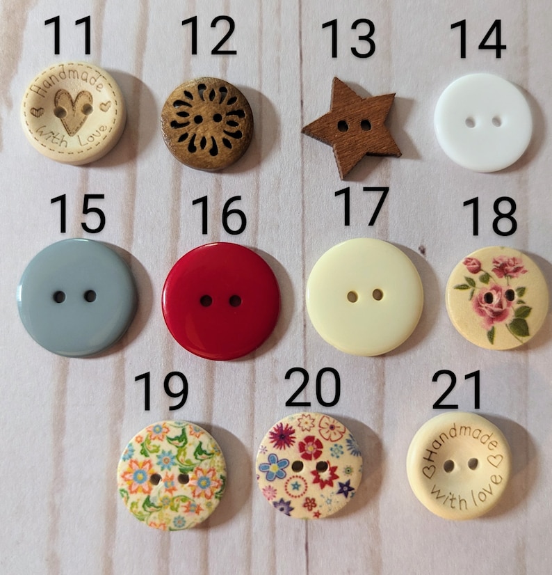 May include: Assortment of 21 different buttons in various colors, patterns, and shapes. The buttons are made of wood, plastic, and fabric. Some buttons have two holes, while others have four holes. The buttons are arranged in a grid pattern on a white surface.