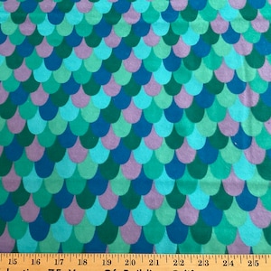 May include: A fabric with a repeating pattern of overlapping teal, green, and purple scales. The fabric is measured with a ruler in inches.
