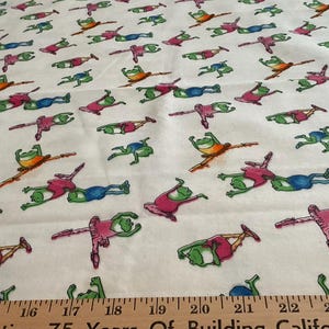May include: White fabric with a repeating pattern of cartoon frogs in various poses. The frogs are in shades of green, orange, blue, and pink. A ruler is at the bottom of the image.