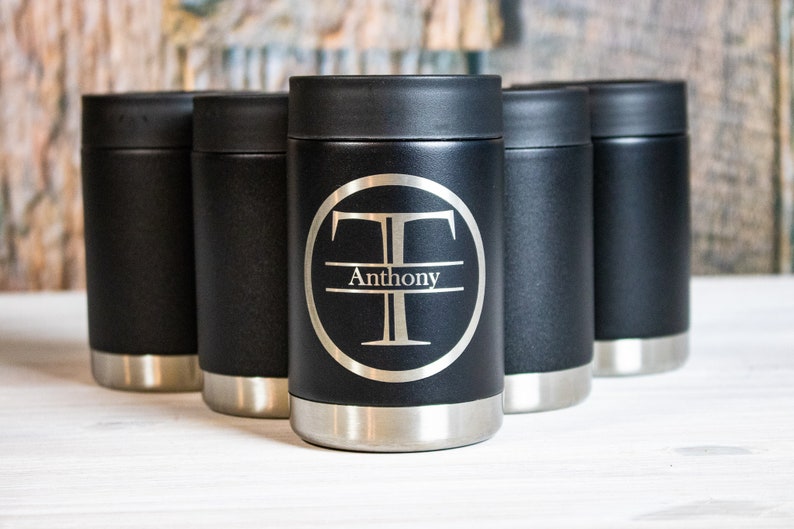 May include: Five black stainless steel insulated beverage holders. One holder has a silver circle with the letter "T" and the name "Anthony" engraved on it.