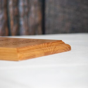 May include: A close-up of the edge of a wooden plaque with a natural wood finish. The plaque is sitting on a white surface.