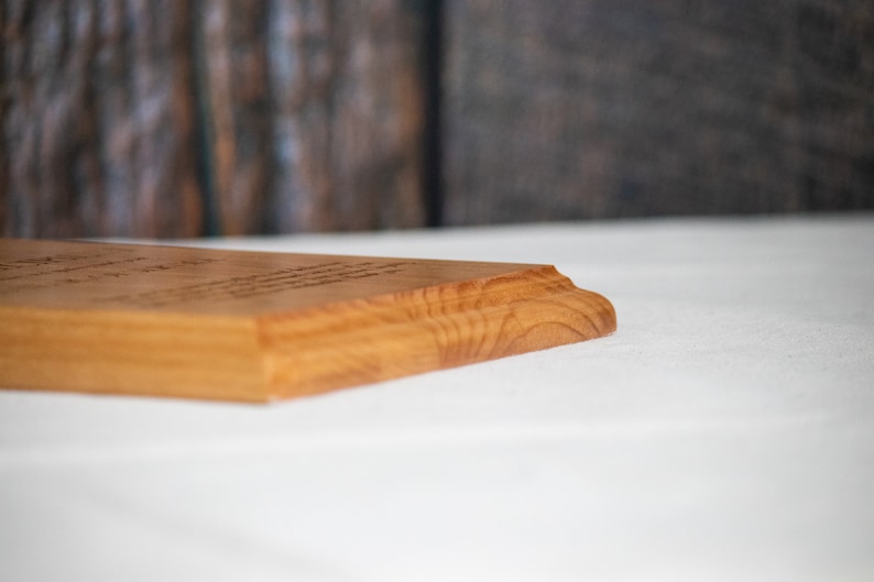 May include: A close-up of the edge of a wooden plaque with a natural wood finish. The plaque is sitting on a white surface.