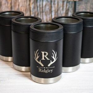 May include: Five black and silver insulated can coolers with a personalized design. The design features a stag's antlers with the letter "R" in the center and the name "Ridgley" below.