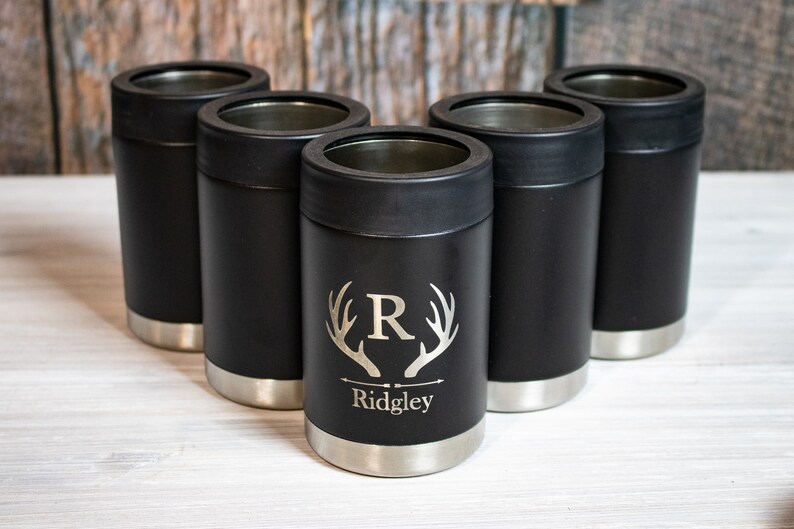 May include: Five black and silver insulated can coolers with a personalized design. The design features a stag's antlers with the letter "R" in the center and the name "Ridgley" below.