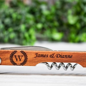 May include: A wooden and metal bottle opener with a corkscrew, a bottle opener, and a knife. The handle is engraved with the text "James & Dianne" and a wreath with the letter "W" inside.