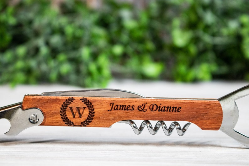 May include: A wooden and metal bottle opener with a corkscrew, a bottle opener, and a knife. The handle is engraved with the text "James & Dianne" and a wreath with the letter "W" inside.