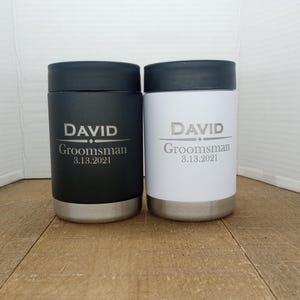 May include: Two stainless steel beverage coolers with black and white lids. The coolers are personalized with the name "DAVID" and the text "Groomsman 3.13.2021".