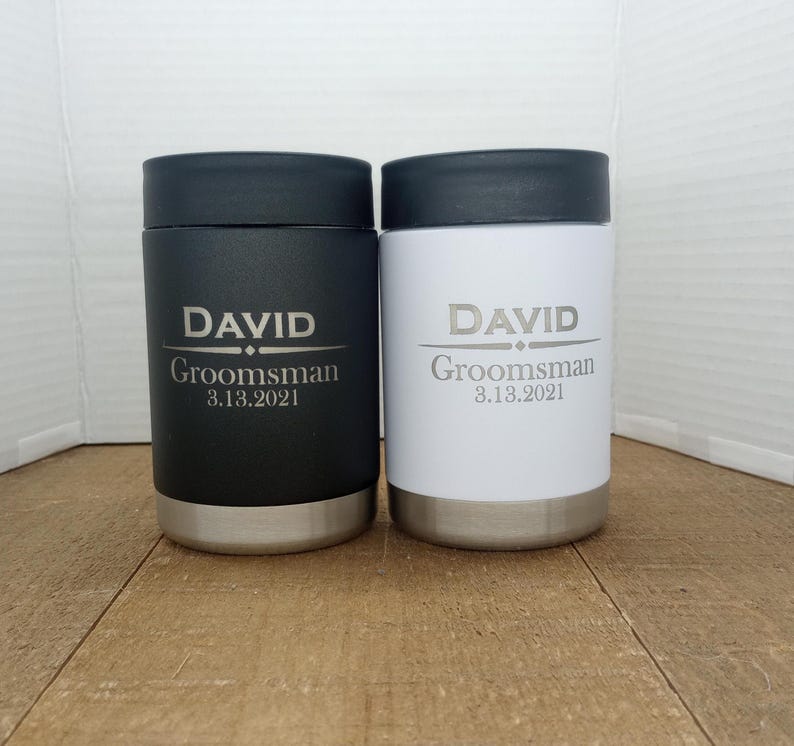May include: Two stainless steel beverage coolers with black and white lids. The coolers are personalized with the name "DAVID" and the text "Groomsman 3.13.2021".