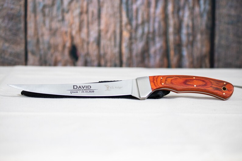 May include: A personalized hunting knife with a red wood handle and a stainless steel blade. The blade is engraved with the name "DAVID" and the text "Groom - 10.10.2020".