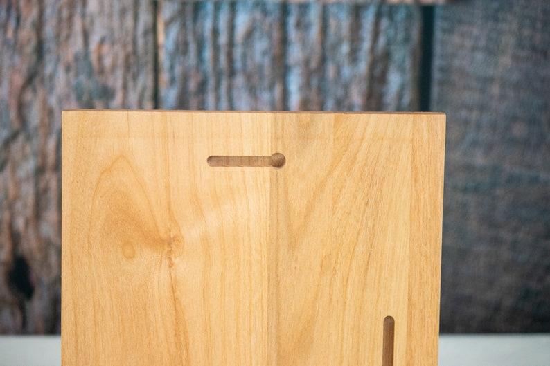 May include: The back of a light wood plaque with two keyhole slots for hanging. The wood has a natural grain pattern.
