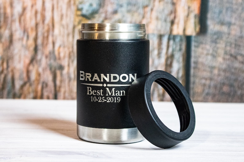 May include: Black insulated can cooler with a silver lid and a black rubber ring. The cooler is engraved with the text "BRANDON Best Man 10-25-2019".