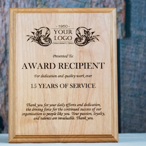 May include: A wooden plaque with a brown stain and a beveled edge. The plaque has an engraved design with a company logo, the text "YOUR LOGO", and the text "CINCINNATL OHIO". The plaque also has the text "Presented To:", "AWARD RECIPIENT", "For dedication and quality work over", "15 YEARS OF SERVICE", and "Thank you for your daily efforts and dedication, the driving force for the continued success of our organization is people like you. Your passion, loyalty, and talents are invaluable. Thank you."