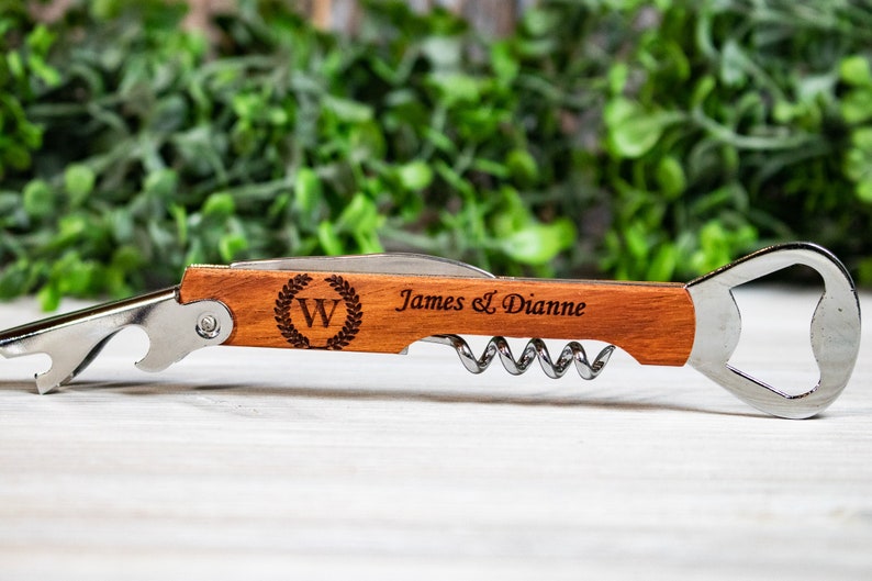 May include: A wooden bottle opener with a corkscrew and a bottle opener. The handle is engraved with the letter "W" in a wreath, and the text "James & Dianne".