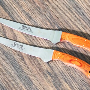 May include: Two personalized steak knives with wooden handles. The blades are engraved with the names "BRIAN" and "DAVID" along with the titles "Groom" and "Groomsman" and the date "10.10.2020".