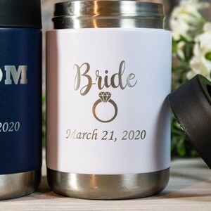 Pu&ograve; includere: Due portabevande in acciaio inox con incisioni personalizzate. Il portabevande blu dice "Groom" con un papillon e "March 21, 2020". Il portabevande bianco dice "Bride" con un anello di diamanti e "March 21, 2020".