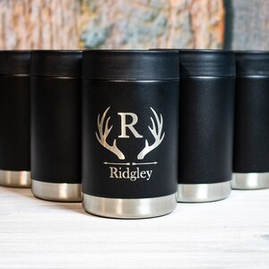 May include: Set of six black stainless steel can coolers with a personalized design. The cooler features a silver stag antler graphic with an initial "R" and the name "Ridgley" engraved on the front.