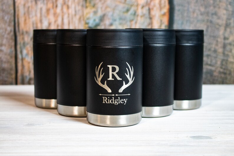 May include: Set of six black stainless steel can coolers with a personalized design. The cooler features a silver stag antler graphic with an initial "R" and the name "Ridgley" engraved on the front.