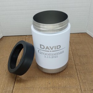 May include: White stainless steel can cooler with a black lid. The cooler has the name "DAVID" and the text "Groomsman 3.13.2021" engraved on it.
