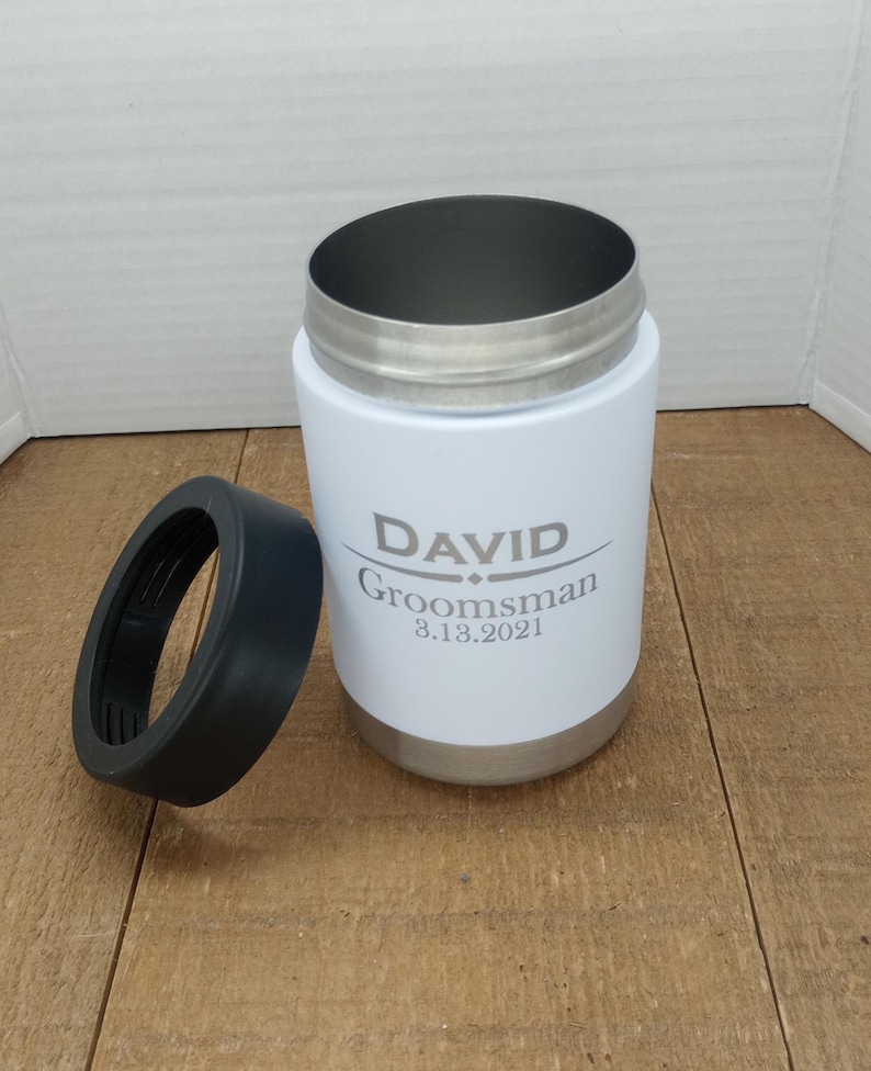 May include: White stainless steel can cooler with a black lid. The cooler has the name "DAVID" and the text "Groomsman 3.13.2021" engraved on it.