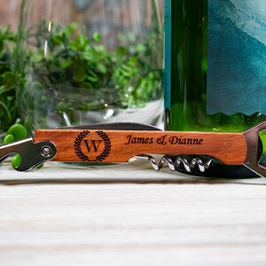 May include: A wooden bottle opener with a corkscrew and a bottle opener. The handle is engraved with the letter "W" in a wreath, and the text "James & Dianne".