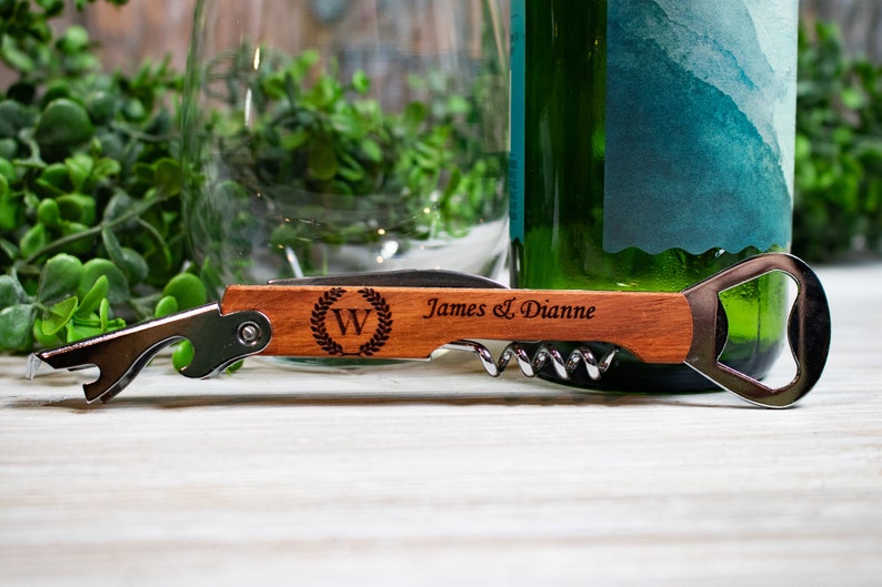 May include: A wooden bottle opener with a corkscrew and a bottle opener. The handle is engraved with the letter "W" in a wreath, and the text "James & Dianne".
